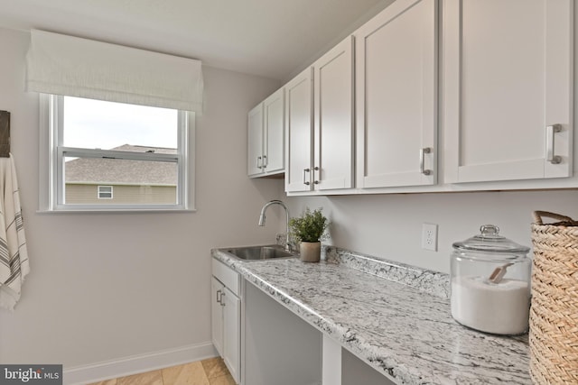 kitchen featuring light stone countertops, sink, white cabinets, and light wood-type flooring