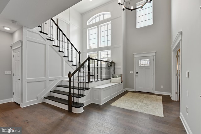 entrance foyer with dark hardwood / wood-style flooring, a towering ceiling, and an inviting chandelier