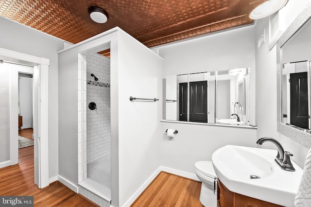 bathroom with toilet, hardwood / wood-style floors, vanity, and a tile shower