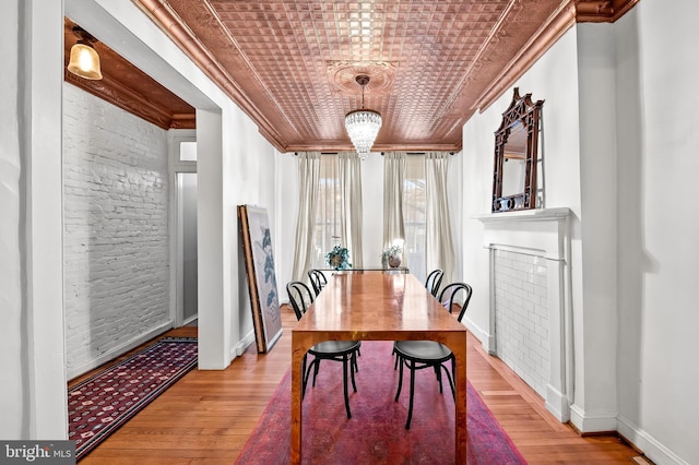 dining room with wood-type flooring, an inviting chandelier, crown molding, and brick wall