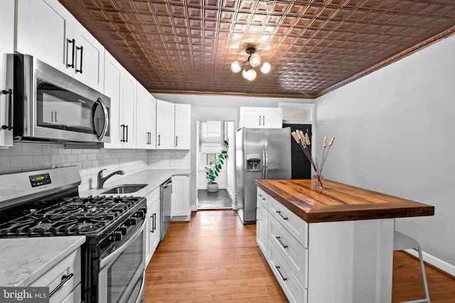 kitchen with butcher block counters, stainless steel appliances, light wood-type flooring, white cabinets, and ornamental molding