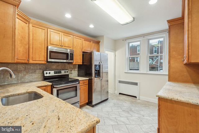 kitchen featuring backsplash, radiator, sink, light stone counters, and stainless steel appliances