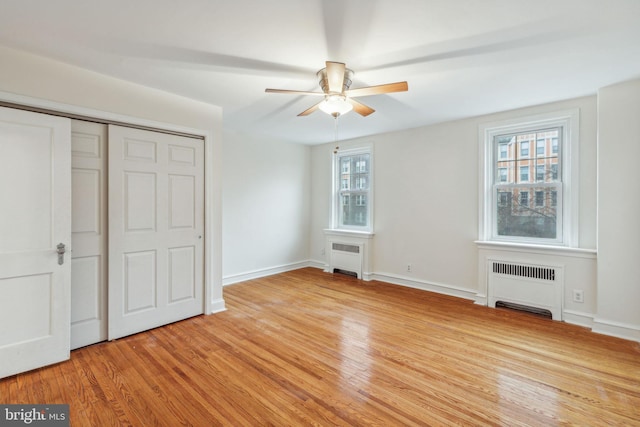 unfurnished bedroom with radiator, ceiling fan, multiple windows, and light wood-type flooring