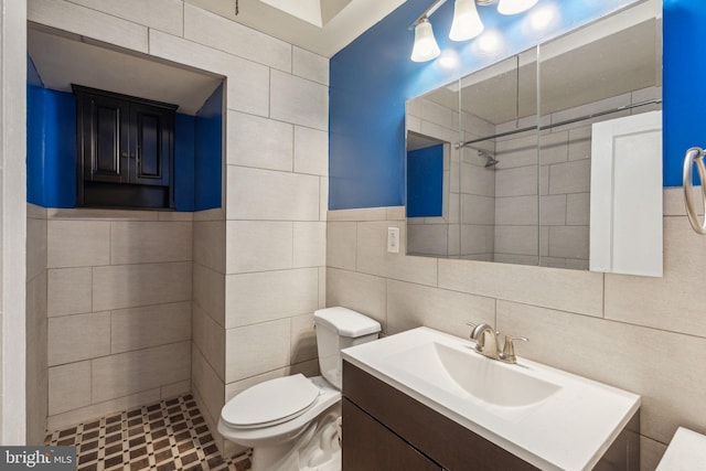 bathroom with tiled shower, vanity, tile walls, and toilet