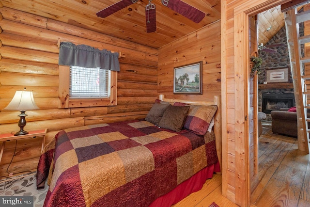 bedroom with hardwood / wood-style floors, a stone fireplace, vaulted ceiling with beams, rustic walls, and wood ceiling