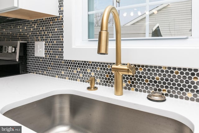 interior details with decorative backsplash, white cabinetry, and sink