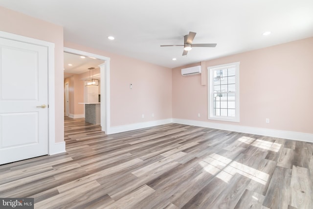 empty room with ceiling fan, light wood-type flooring, and a wall mounted AC