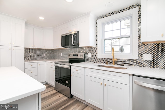 kitchen featuring white cabinetry, sink, light hardwood / wood-style floors, decorative backsplash, and appliances with stainless steel finishes