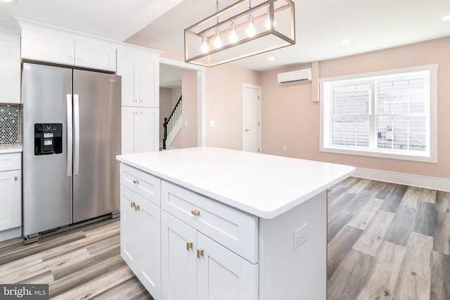 kitchen featuring an AC wall unit, stainless steel fridge, white cabinets, and decorative light fixtures