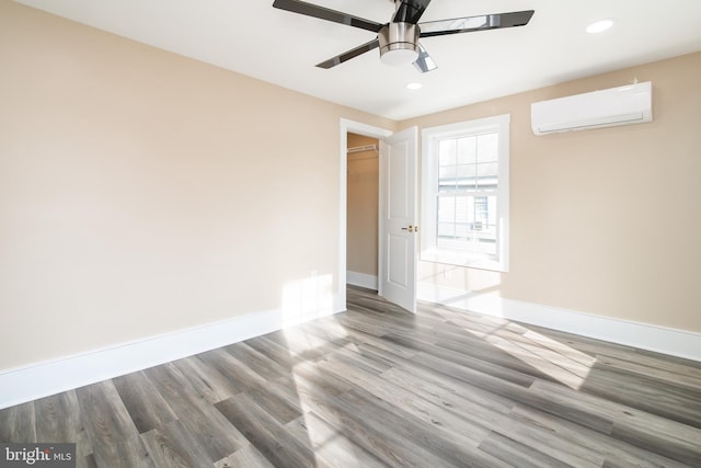 spare room featuring wood-type flooring, an AC wall unit, and ceiling fan