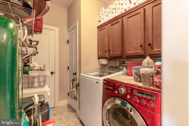 clothes washing area with washing machine and dryer, light tile patterned floors, and cabinets