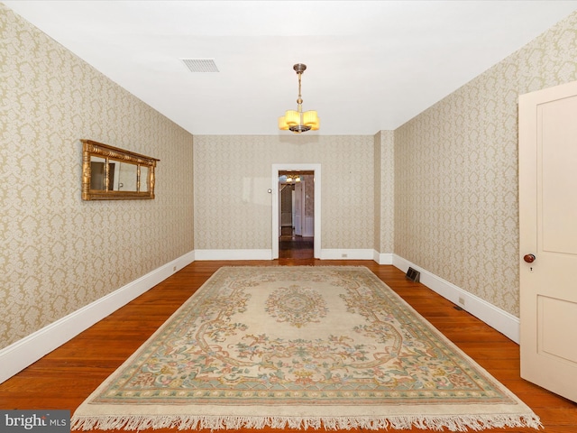 empty room with baseboards, wood finished floors, visible vents, and wallpapered walls