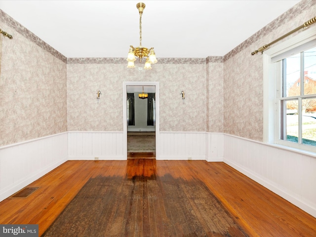 unfurnished dining area with a wainscoted wall, hardwood / wood-style floors, a chandelier, and wallpapered walls