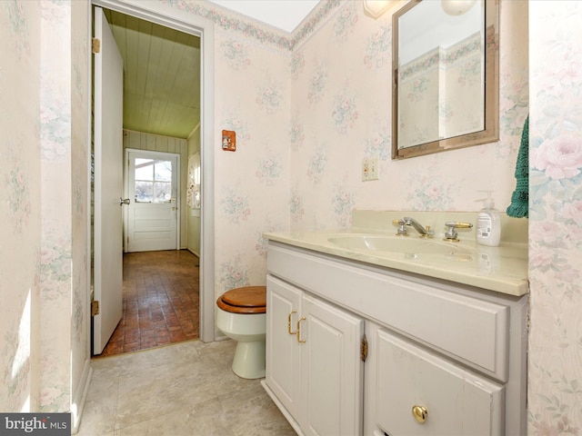 bathroom featuring toilet, wallpapered walls, and vanity