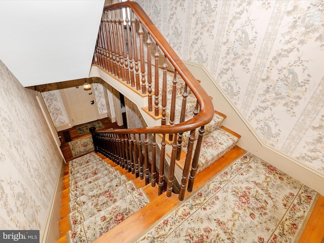 stairs with wallpapered walls and wood finished floors