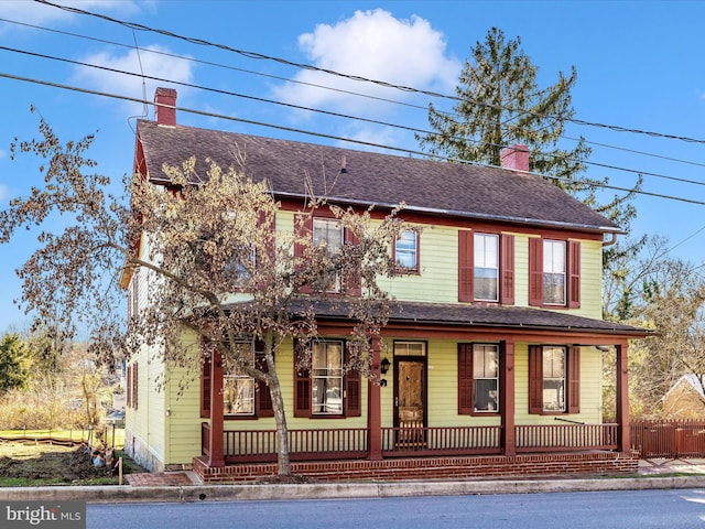 view of front of property with a porch, a chimney, a shingled roof, and fence