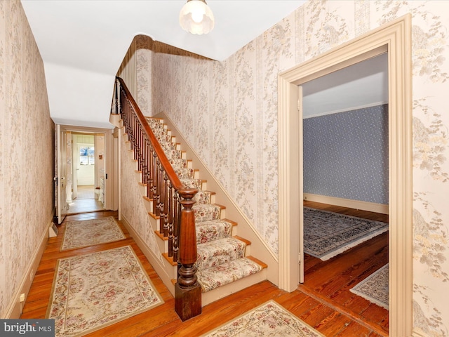 staircase featuring baseboards, wood finished floors, and wallpapered walls