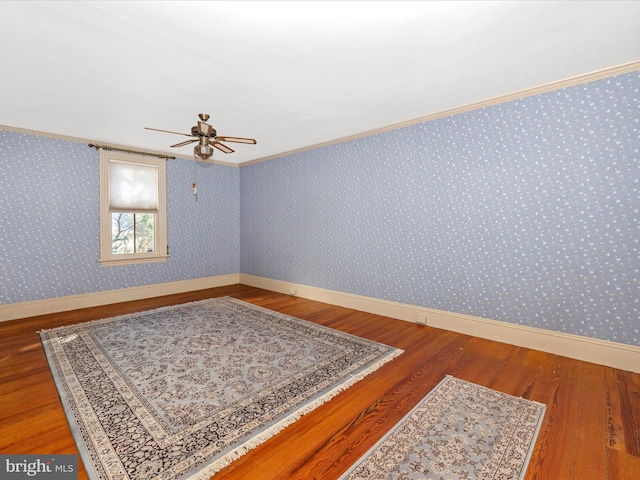 empty room with wallpapered walls, baseboards, wood finished floors, and ornamental molding