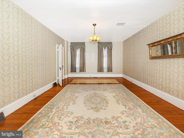 spare room featuring baseboards, wood finished floors, and wallpapered walls