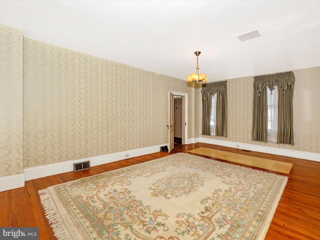 unfurnished room featuring wallpapered walls, baseboards, visible vents, and hardwood / wood-style flooring