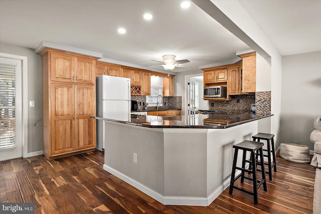 kitchen with kitchen peninsula, decorative backsplash, ceiling fan, white fridge, and dark hardwood / wood-style floors