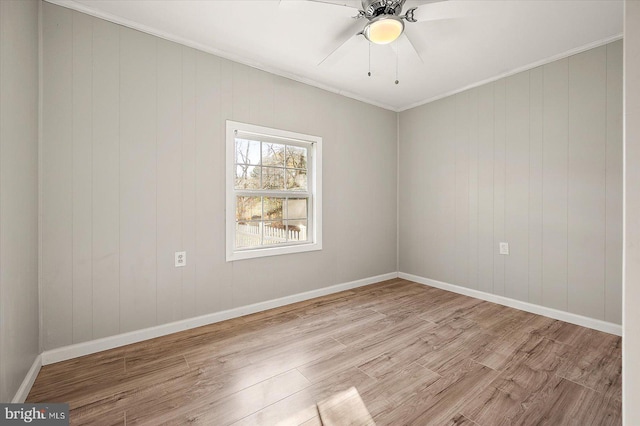 spare room featuring ceiling fan, crown molding, wooden walls, and light wood-type flooring