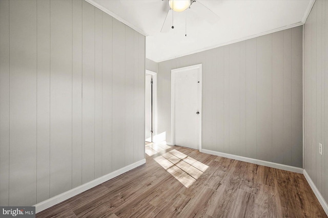 unfurnished room with ceiling fan, ornamental molding, wooden walls, and light hardwood / wood-style flooring