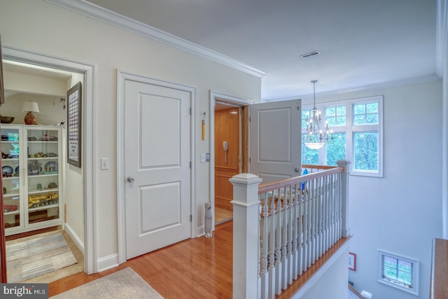 hallway featuring an inviting chandelier, ornamental molding, and light wood-type flooring