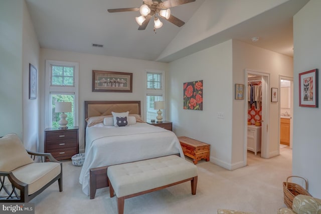 bedroom featuring ceiling fan, ensuite bathroom, light colored carpet, vaulted ceiling, and a walk in closet