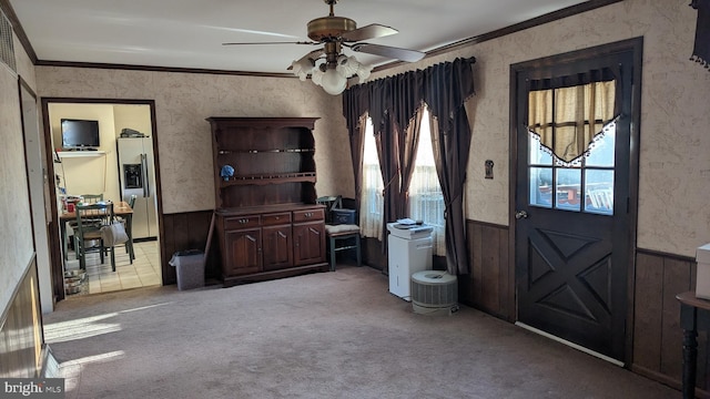 carpeted foyer with ceiling fan, crown molding, and wood walls