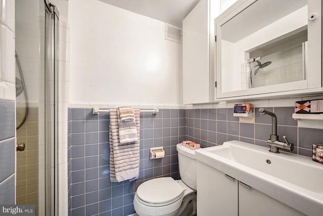 bathroom featuring a shower with door, vanity, tile walls, and toilet