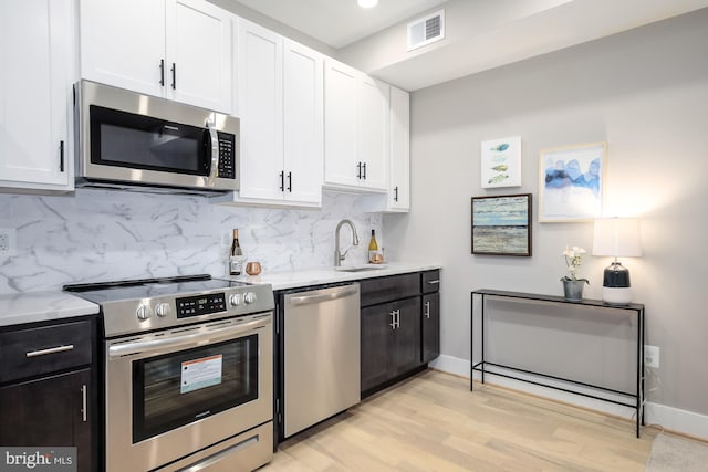 kitchen with light wood-type flooring, stainless steel appliances, white cabinetry, and tasteful backsplash