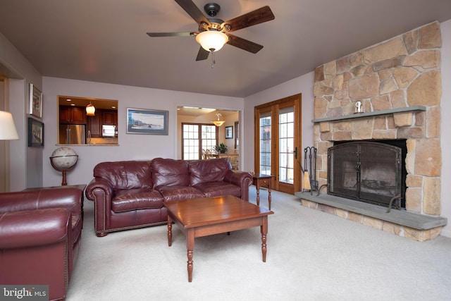 carpeted living room with a stone fireplace and ceiling fan