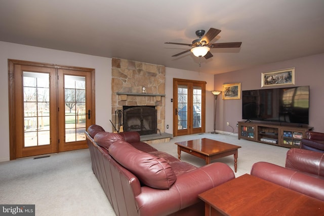 carpeted living room with a stone fireplace, ceiling fan, french doors, and a healthy amount of sunlight