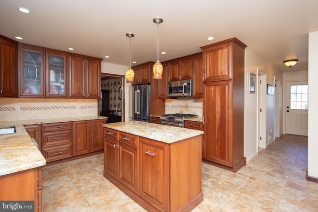 kitchen featuring backsplash, light stone counters, stainless steel appliances, decorative light fixtures, and a kitchen island