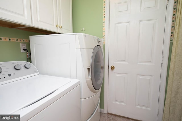 clothes washing area featuring washer and dryer, light tile patterned flooring, and cabinets