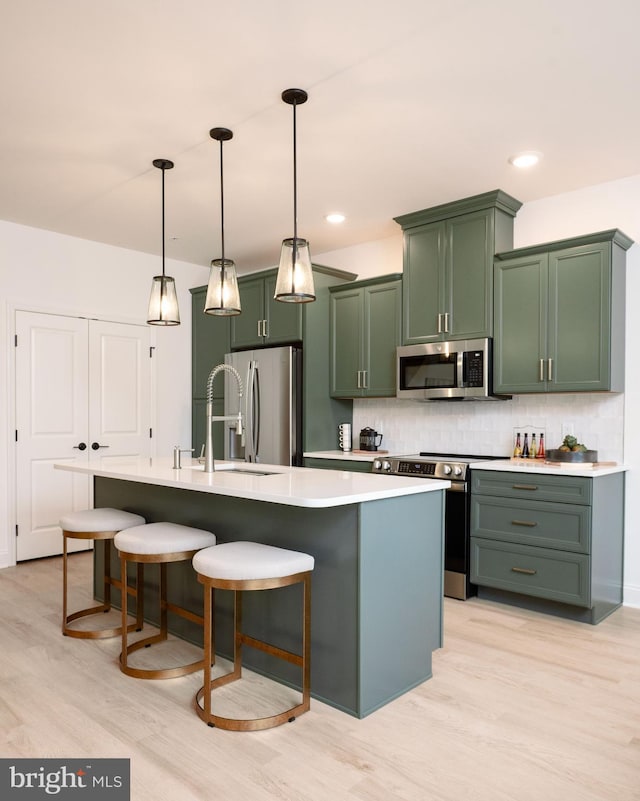 kitchen with a center island with sink, light hardwood / wood-style flooring, appliances with stainless steel finishes, tasteful backsplash, and decorative light fixtures