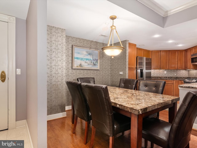 dining space with ornamental molding and light hardwood / wood-style flooring