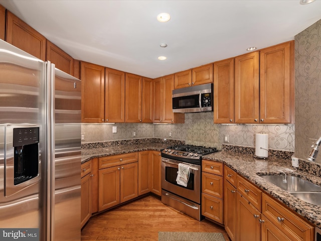 kitchen with dark stone countertops, stainless steel appliances, light hardwood / wood-style floors, and sink