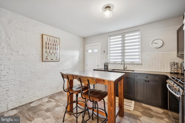 kitchen featuring dark brown cabinets, high end range, sink, and brick wall