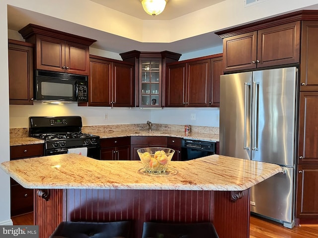 kitchen with a breakfast bar, a center island, black appliances, light stone countertops, and light wood-type flooring