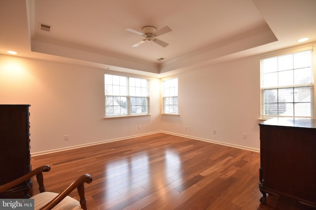 interior space featuring ceiling fan, a raised ceiling, ornamental molding, and dark wood-type flooring