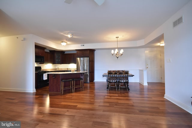 kitchen featuring dark brown cabinetry, a center island, hanging light fixtures, dark wood-type flooring, and black appliances