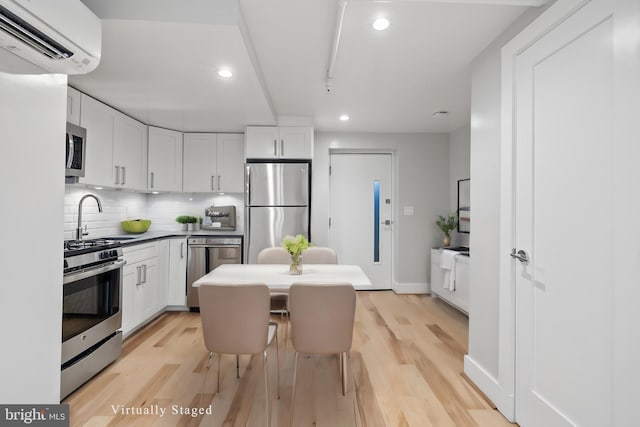 kitchen featuring stainless steel appliances, a wall unit AC, sink, light hardwood / wood-style floors, and white cabinetry