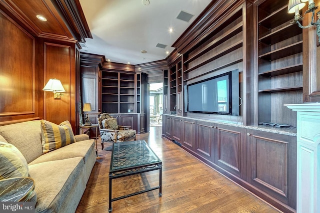 living room with crown molding, built in features, wood-type flooring, and wooden walls