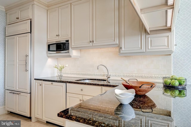 kitchen with backsplash, built in appliances, dark stone countertops, and sink