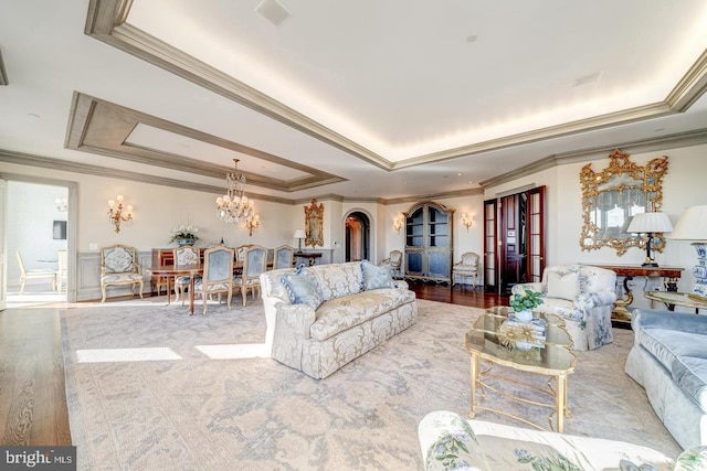 living room with a tray ceiling, crown molding, an inviting chandelier, and hardwood / wood-style flooring