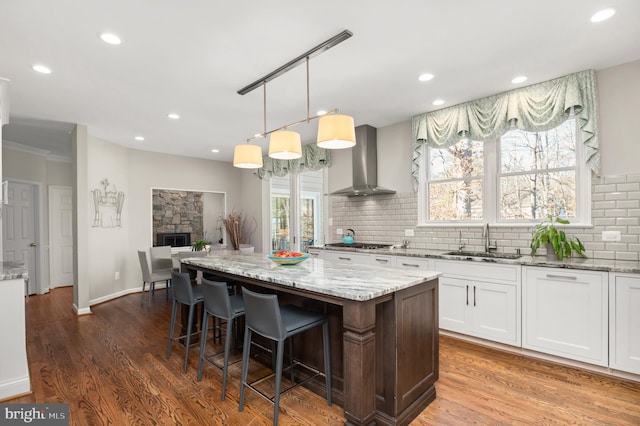 kitchen with white cabinetry, sink, a center island, light stone countertops, and wall chimney range hood