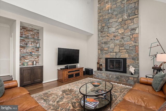 living room with dark hardwood / wood-style floors, ornamental molding, and a stone fireplace