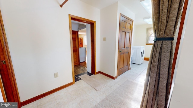 hall featuring light tile patterned floors, washing machine and dryer, and baseboards